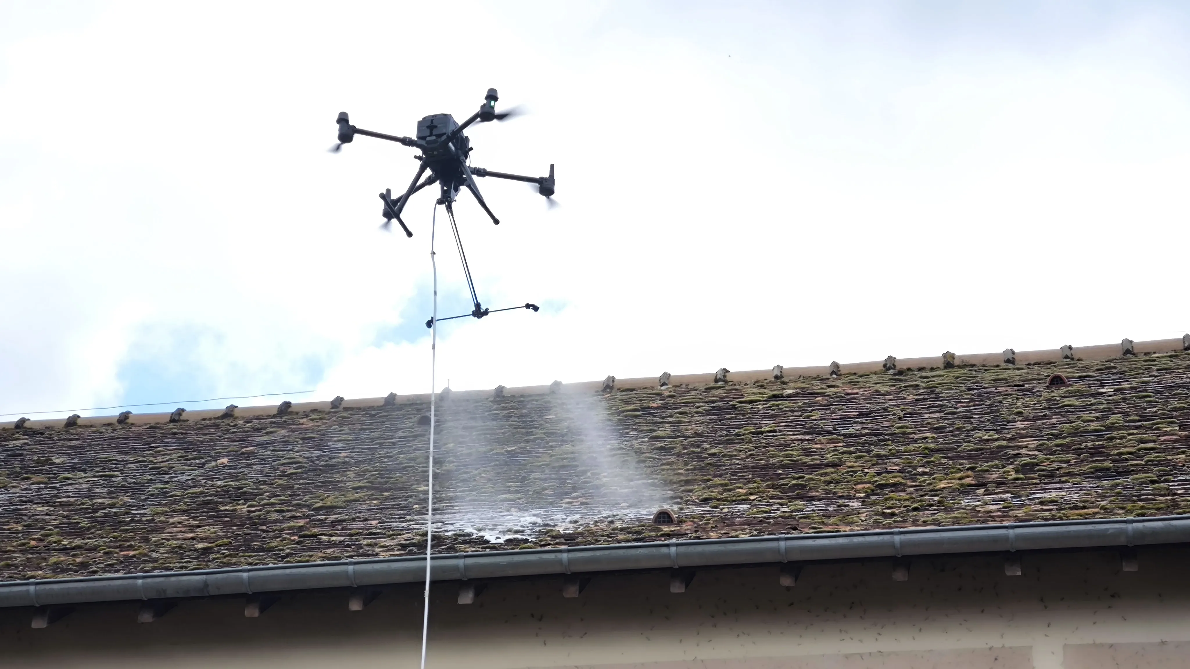 Drone CLEANALTA en pleine action de pulvérisation sur une toiture en tuile plate moussée, intervention sans échafaudage en Yvelines