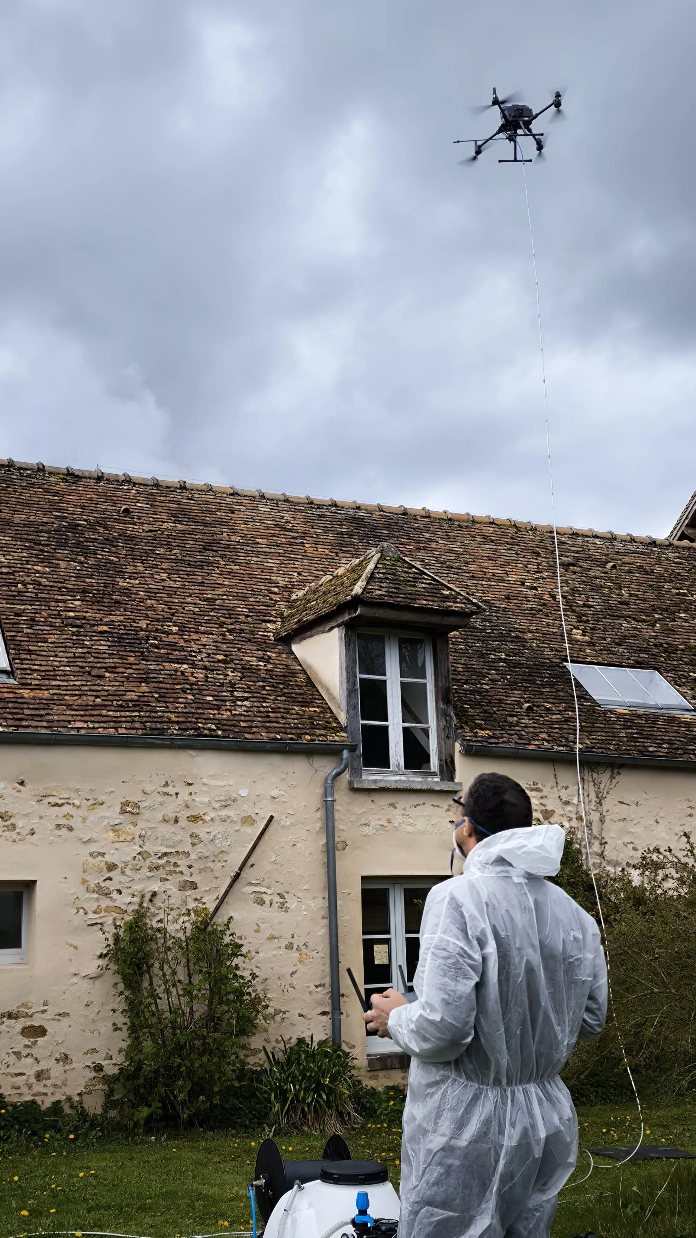 T&eacute;l&eacute;pilote AltaClean en combinaison Tyvek, EPI complet, drone en vol sur long&egrave;re ancienne